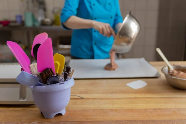 Hamur işlerini hazırlayan bir pasta şefinin arka planında plastik bir kapta spatulalar.