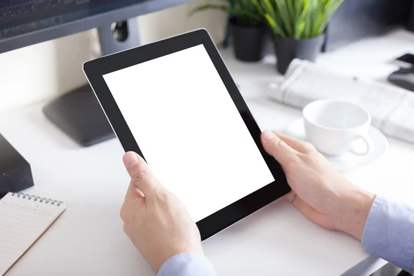 Mãos de um homem segurando dispositivo tablet em branco sobre uma tabl espaço de trabalho — Fotografia de Stock