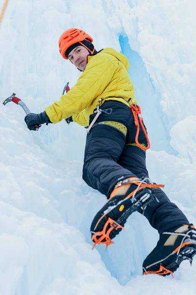 Athletic alpinist man in orange helmet and ice tools axe climbing a large wall of ice. Outdoor Sports Portrait — Stock Photo, Image