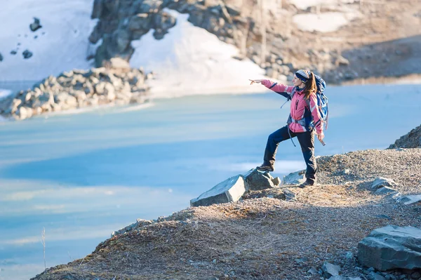 Une jeune femme avec un sac à dos pointe au loin sur la rive d'un lac gelé — Photo
