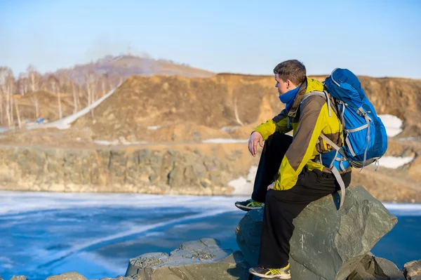 Un jeune homme avec un sac à dos assis sur le bord du lac d'automne — Photo