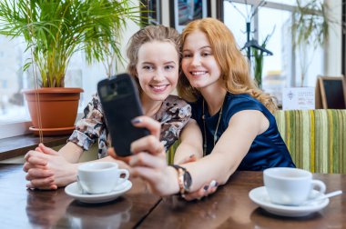 selfie. İki güzel gülümseyen kız dışında kafede bir smartphone fotoğrafı