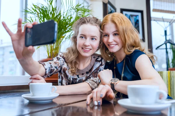Selfie. Dos hermosas chicas sonrientes fotografiadas en un teléfono inteligente en la cafetería exterior — Foto de Stock