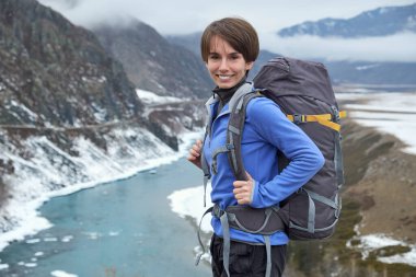 Sırt çantasıyla dağlarda gezen gülümseyen bir kadın. Güzel genç kız dağlarda geziyor.