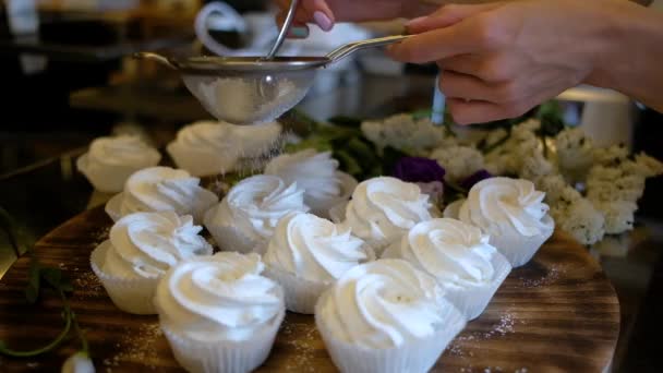 Confitero espolvorea azúcar helada con el postre. El azúcar en polvo cae sobre los cupcakes — Vídeo de stock