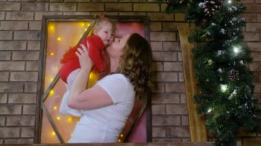 Mutlu anne odada Noel ağacı süslemelerinin yanında bebekle oynuyor.