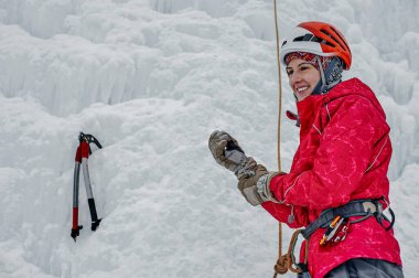Elinde buz aletleri olan, turuncu kasklı baltası olan dağcı kadın büyük buz duvarına tırmanıyor. Açık hava Spor Portresi