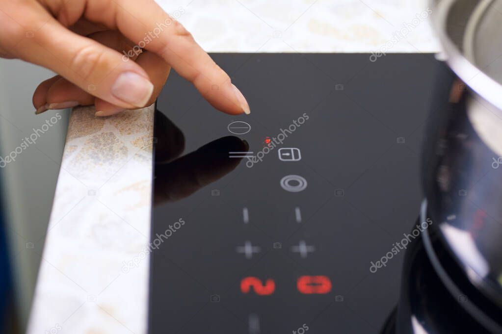 Woman hand includes modern induction stove in kitchen