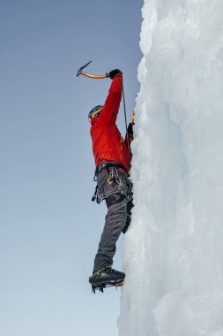 Buzdan aletleri olan buz tırmanışçısı baltayla büyük bir buz duvarına tırmanıyor. Evet.