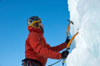 Elinde buz aletleri olan dağcı adam baltayla büyük bir buz duvarına tırmanıyor. Açık hava Spor Portresi