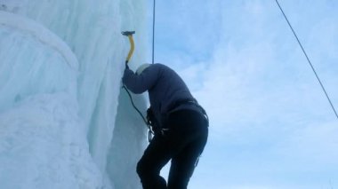 Buz aletli dağcı baltayla büyük bir buz duvarına tırmanıyor..