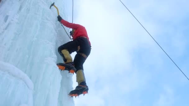 Alpinist man med is verktyg yxa klättra en stor vägg av is. — Stockvideo