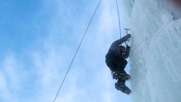 Hombre alpinista con hacha de herramientas de hielo escalando una gran pared de hielo. — Vídeo de stock
