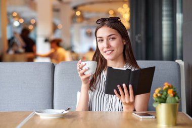 Bir kafede kitap okuyan ve kahve içen genç bir kadın..