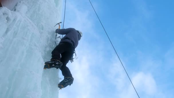 Alpinist man med is verktyg yxa klättra en stor vägg av is. — Stockvideo