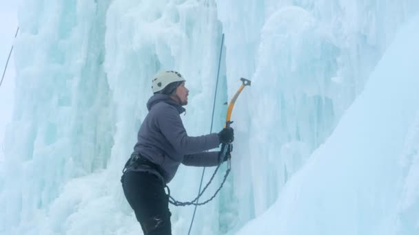 Alpinist man med is verktyg yxa klättra en stor vägg av is. — Stockvideo