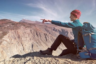 Sırt çantalı bir yürüyüşçü dağın tepesinde duruyor, elleri havada ve güneşin doğuşunun keyfini çıkarıyor.