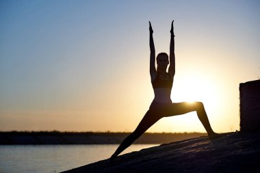 Siluet kadın yoga yapıyor ya da gün batımında ya da gün doğumunda sahilde geriniyor..