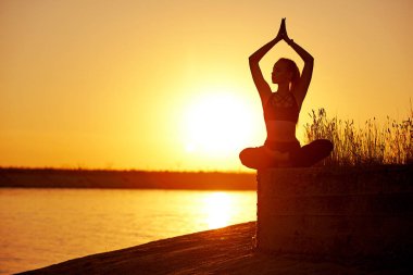 Siluet kadın yoga yapıyor ya da gün batımında ya da gün doğumunda sahilde geriniyor..