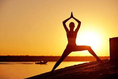 Siluet kadın yoga yapıyor ya da gün batımında ya da gün doğumunda sahilde geriniyor..