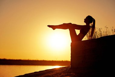 Siluet kadın yoga yapıyor ya da gün batımında ya da gün doğumunda sahilde geriniyor..