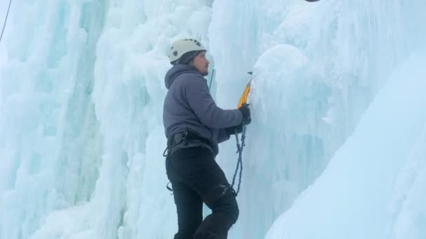 Hombre alpinista con hacha de herramientas de hielo escalando una gran pared de hielo. — Vídeos de Stock