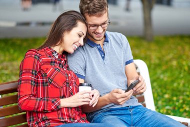 Genç bir çiftin güzel portresi. Bankta oturuyorlar, sarılıyorlar ve öpüşüyorlar..