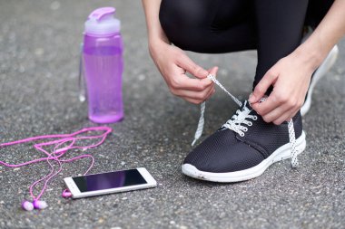 Koşu ayakkabısı bağlayan koşucu kadın koşuya hazırlanıyor stadyumda bir şişe su ve kulaklıkla koşuya hazırlanıyor.