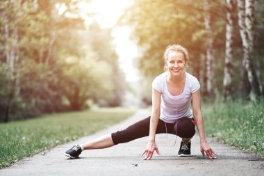 Atletik gözcü kız yaz parkında geriniyor. Açık hava fitness portresi