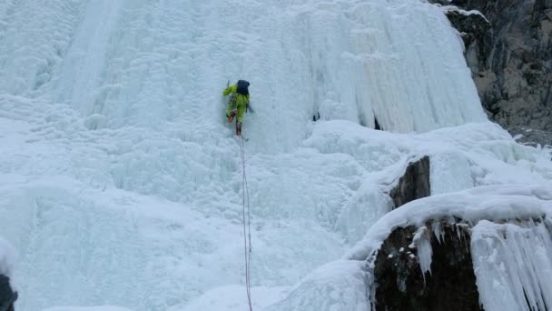 Pria alpen dengan kapak alat es memanjat air terjun beku, dinding besar es — Stok Video