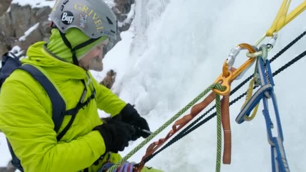Buz aletli dağcı baltayla donmuş bir şelaleye tırmanıyor, büyük bir buz duvarı. — Stok video
