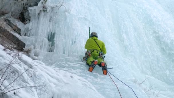 Alpinist man med is verktyg yxa klättra ett fruset vattenfall, en stor vägg av is — Stockvideo