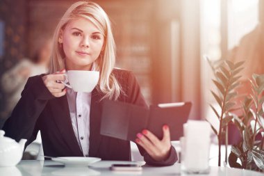 Kafede kitap okuyan ve kahve içen genç bir kadın..