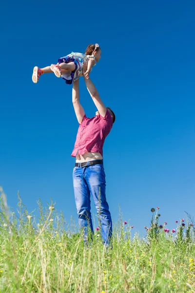 Retrato exterior de un padre que lanza a su hija en el aire contra el cielo — Foto de Stock