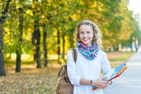 Smiling girl student with folders and books walking in the autumn park — Zdjęcie stockowe