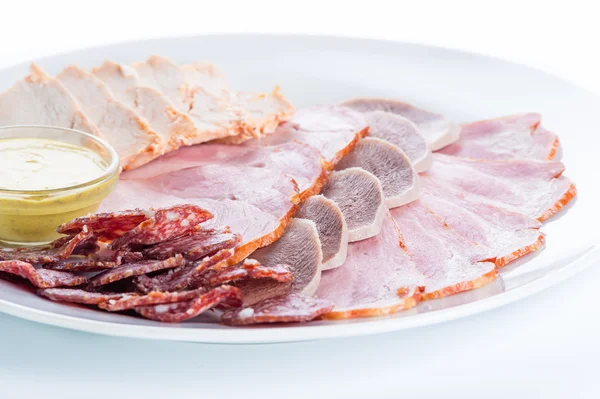 Carne variada: jamón, salchicha ahumada, salami, pollo, lengua y mostaza sobre fondo blanco —  Fotos de Stock