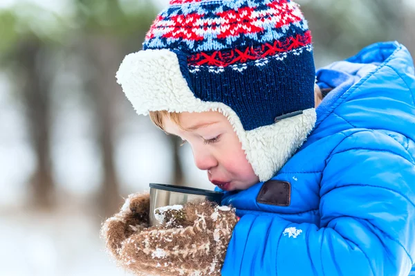 Buiten portret kind blazen op hete thee uit een thermoskan in winter park — Stockfoto