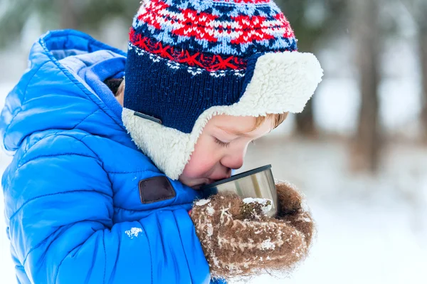 Retrato ao ar livre Criança feliz bebendo chá quente de uma garrafa térmica no parque de inverno — Fotografia de Stock