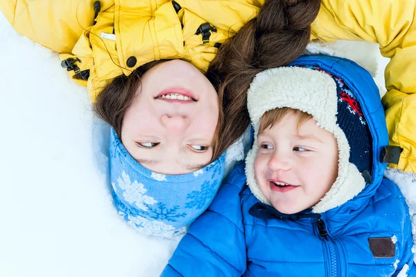 Outdoor portrait Happy mother and baby lying on the snow in winter park and smiling — Stock Photo, Image