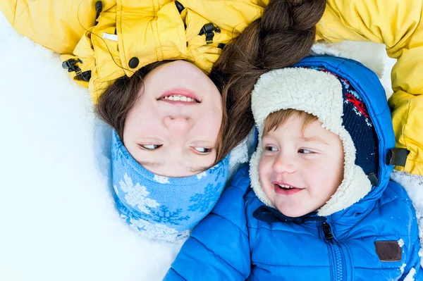 Ritratto all'aperto Madre felice e bambino sdraiato sulla neve nel parco invernale e sorridente Fotografia Stock