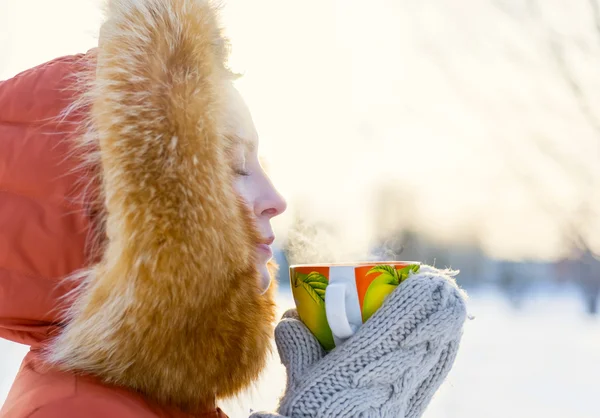 Outdoor Portret van een lachende jong meisje in een bont capuchon. Thee drinken uit een Oranje mok in de winter park — Stockfoto