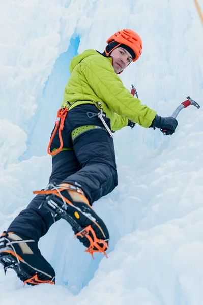 Atletico alpinista uomo in casco arancione e piccozza attrezzi arrampicata su una grande parete di ghiaccio. Ritratto sportivo all'aperto — Foto Stock