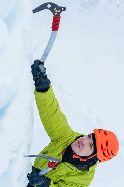 Homme alpiniste athlétique au casque orange et à la hache à outils de glace escaladant un grand mur de glace. Portrait de sport extérieur — Photo