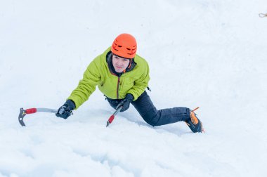 Ice climber man with  ice tools axe in orange helmet climbing a large wall of ice. Outdoor Sports Portrait