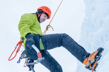 Elinde buz aletleri olan dağcı adam turuncu kasklı baltayla büyük bir buz duvarına tırmanıyor. Açık hava Spor Portresi