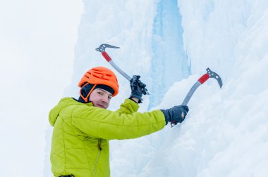Ice climber man with  ice tools axe in orange helmet climbing a large wall of ice. Outdoor Sports Portrait