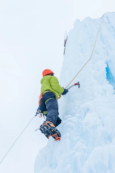 Homme alpiniste avec piolet à outils en casque orange escaladant un grand mur de glace. Portrait de sport extérieur — Photo