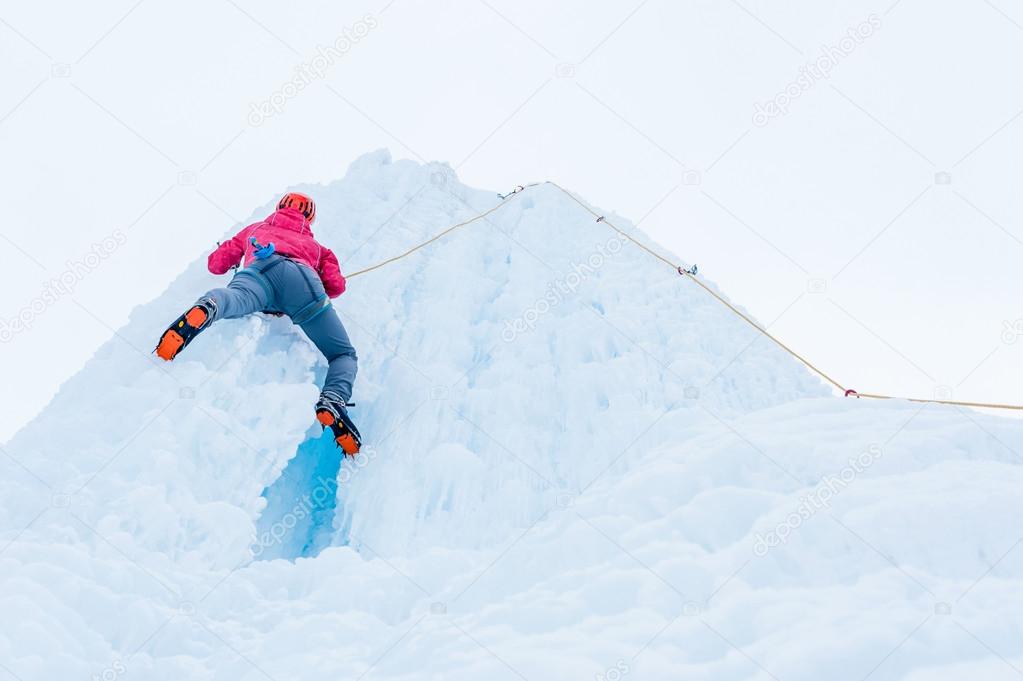 Alpinist woman with  ice tools axe in orange helmet climbing a large wall of ice. Outdoor Sports Portrait