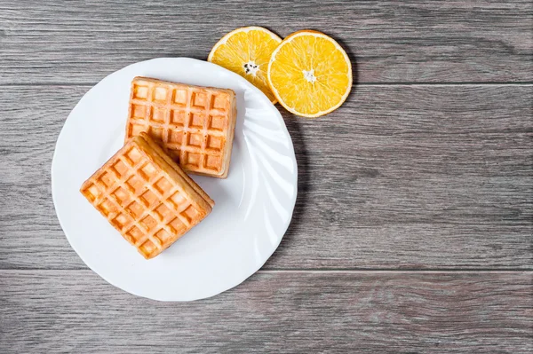 Waffles and dried oranges on a white plate on a wooden background. Place for text. Square image. — Stock Photo, Image