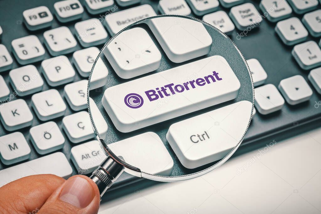 Cryptocurrency trading concept: Male hand holding magnifying glass and focusing computer key with bittorrent | btt logo. Cryptocurrency mining, trading, market concept.